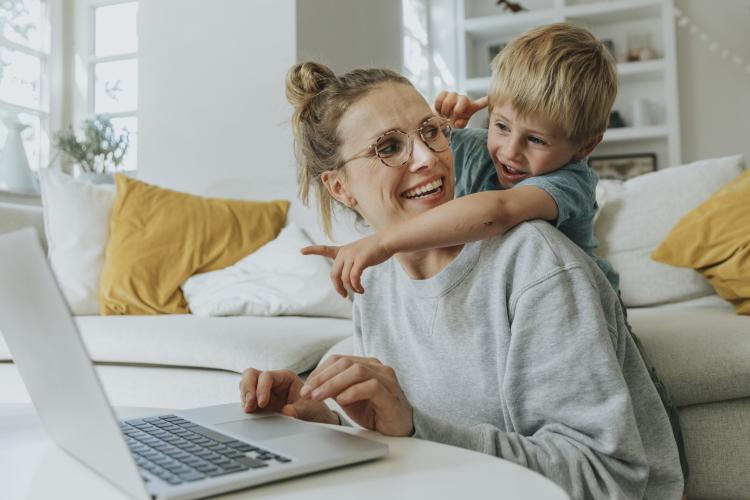 Eine Frau sitzt am Laptop, ihr Sohn umarmt sie und zeigt auf den Bildschirm