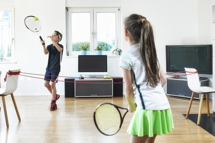 Zwei Kinder spielen in einem Wohnzimmer Tennis